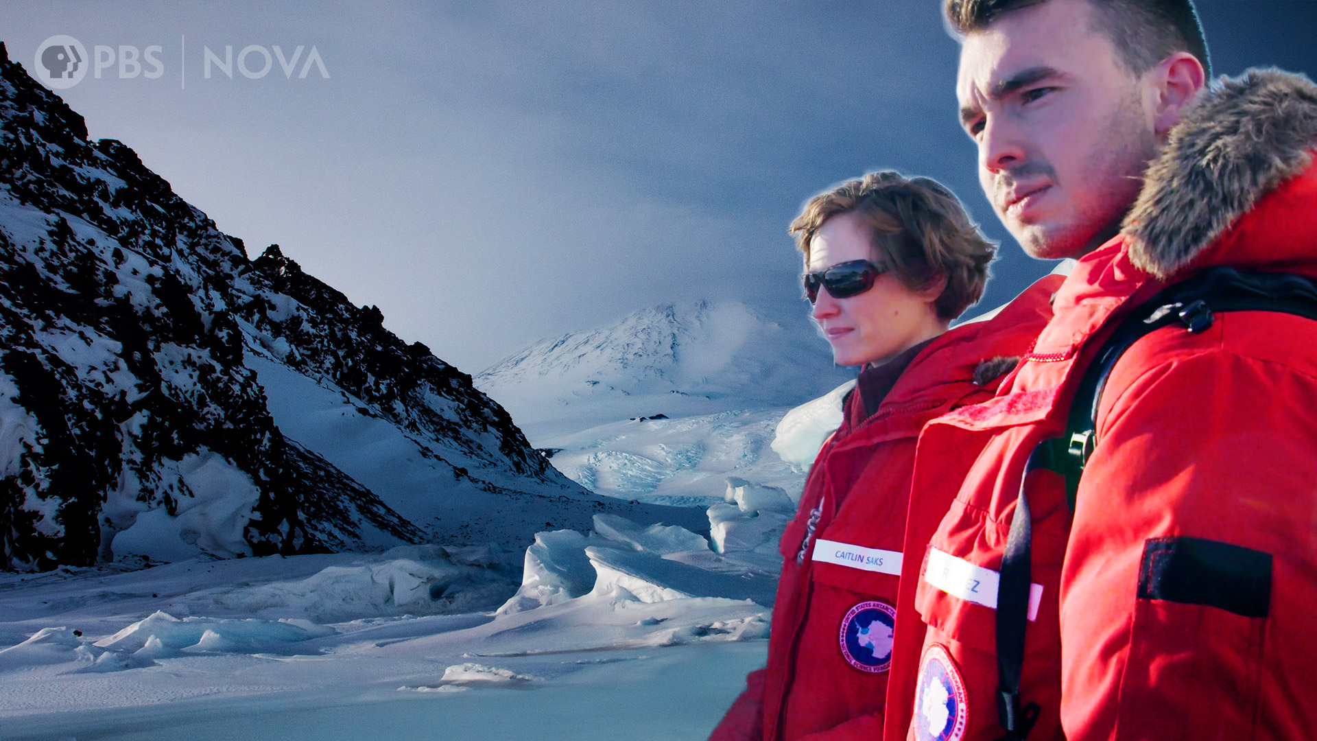 Two people in large coats, with the landscape of Antarctica in the background.