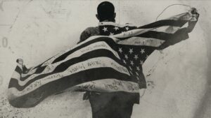 A person, with their back to camera, drapes an American flag over their back, with the flag marked up with several names.
