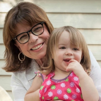 A woman with glasses smiles as she holds a toddler, who is also smiling.