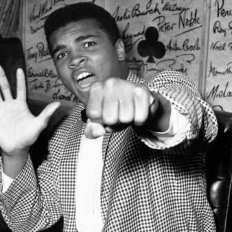 Muhammad Ali holding up a fist and five fingers on the other hand