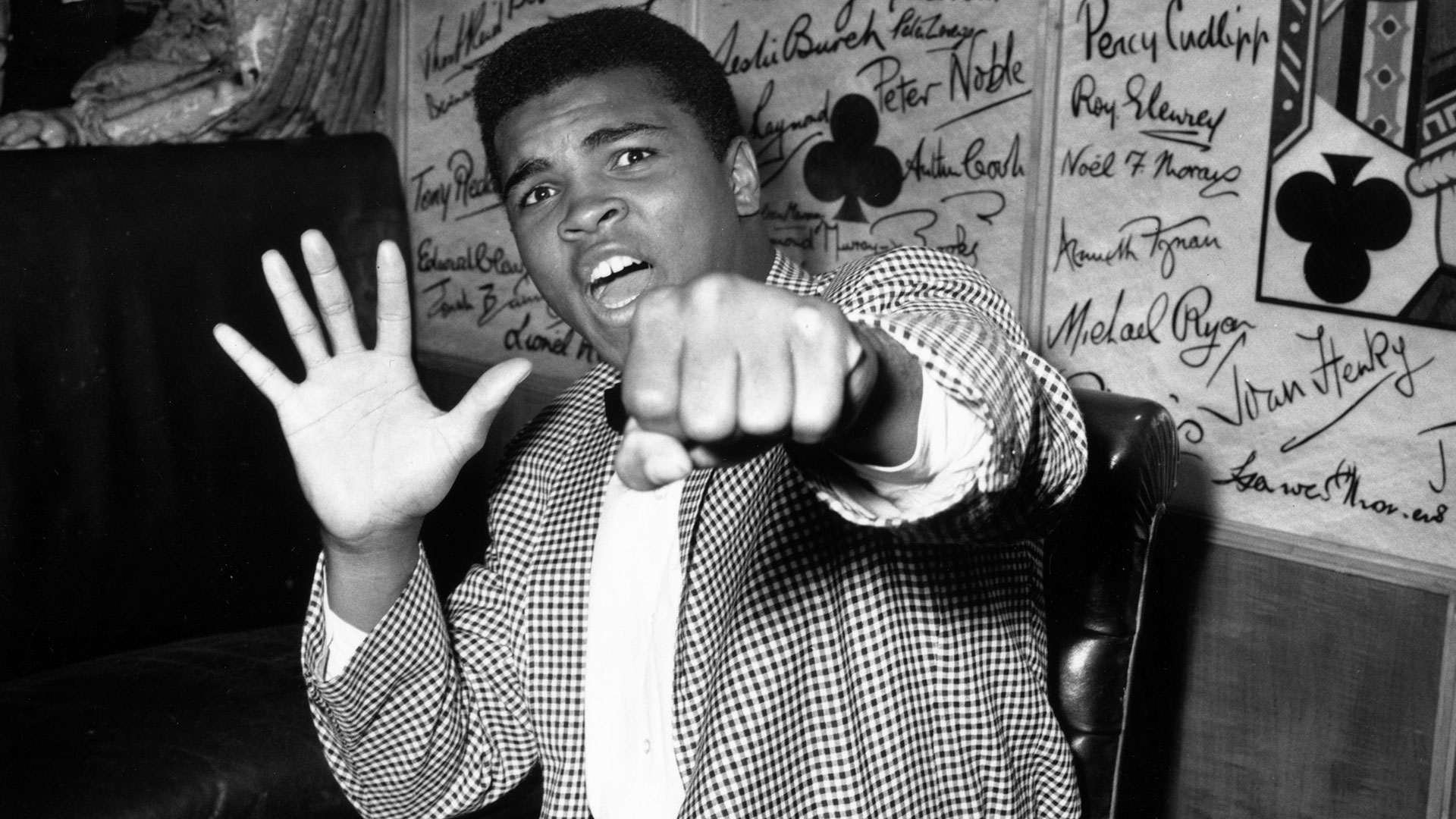 Muhammad Ali holding up a fist and five fingers on the other hand